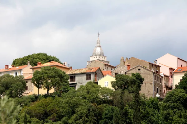 古老的地中海小镇 在当地的天主教教堂周围 到处都是传统的石砌房屋 屋顶上的金属瓦片高高在上 周围是茂密的树木和乌云密布的蓝天 — 图库照片