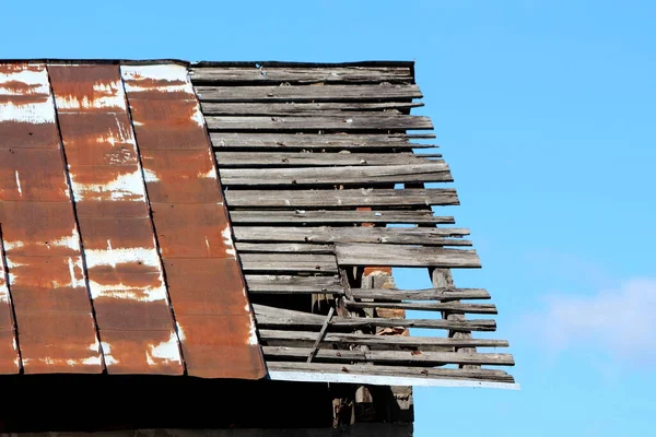 錆びた金属製の屋根タイルと目に見える割れ目の壊れた木製の板を持つ放棄された家族の家の屋根を破壊しました澄んだ青空の背景に錆びた釘と一緒に開催 — ストック写真