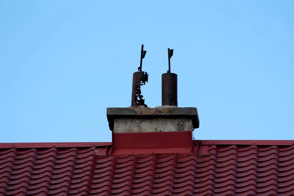 上に2つの狭い錆びた金属パイプを持つデュアル老朽化したコンクリート煙突は 澄んだ青い空の背景に改装された新しい赤い屋根のタイルで囲まれています — ストック写真