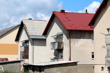 Benzer banliyö aile evleri eski harap olmuş cephe ve yenilenmiş çatı beton yapı bloklarının yanında yeni kırmızı kiremitler bulutlu mavi gökyüzü arka planında açık hava depolama kulübeleri
