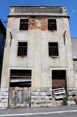 Geleneksel taş temelde, çok eski kırmızı tuğlalar, kırık cephe ve metal parmaklıkların üzerinde eksik camlar tahtadan yapılmış tahtadan yapılmış, yıkık kapılar, eğimli, mavi gökyüzü sırtındaki kaldırımlı caddenin hemen yanında.