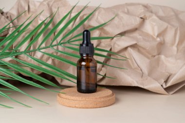 Bir CBD yüz serumu ya da kahverengi bir damlacık şişesinde yağlı ve yanında yeşil bir yaprak olan bir el işi kağıdı arka planında.