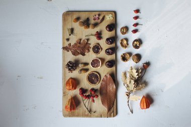 Yapraklar, fındıklar, böğürtlenler, koniler ve kuru portakallarla dolu sonbahar yaşam kompozisyonu beyaz masanın üstündeki ahşap tahta üzerinde, mevsimlik dekorasyon konsepti, üst görünüm