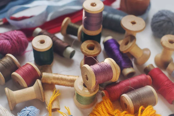 Sewing tools, vintage wooden bobbins with colorful thread on white table, selective focus