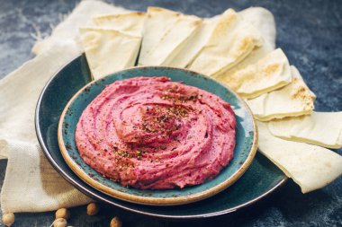 Ev yapımı pancar humusu, nohut ve pide dilimleri koyu taş masada mavi tabakta. Geleneksel ortadoğu yemeği, seçici odak