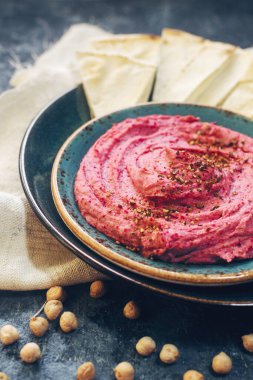 Ev yapımı pancar humusu, nohut ve pide dilimleri koyu taş masada mavi tabakta. Geleneksel ortadoğu yemeği, seçici odak