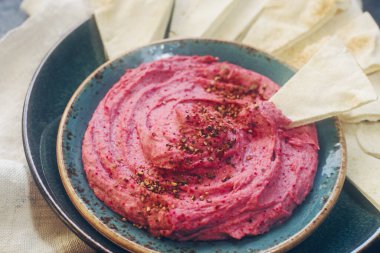 Ev yapımı pancar humusu, nohut ve pide dilimleri koyu taş masada mavi tabakta. Geleneksel ortadoğu yemeği, seçici odak