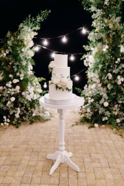 Beyaz çiçeklerle süslenmiş beyaz düğün pastası. Pasta akşam kemerinin arka planında duruyor. Yüksek kalite fotoğraf