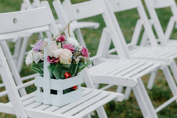 Een ruiker van bloemen in een van hout keet staat op witte stoelen — Stockfoto