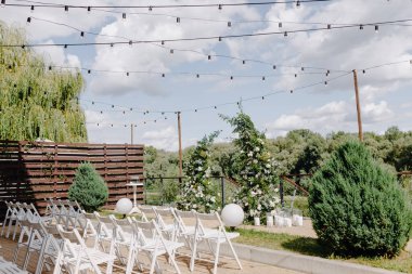 Yazın, bulutların ve ağaçların arka planındaki düğün alanı kompozisyon ve çiçeklerle süslenir.