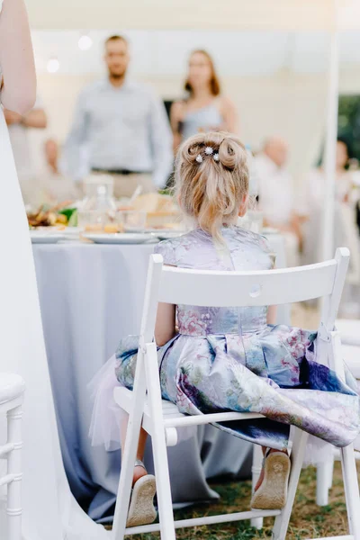 Elbiseli güzel küçük kız bir restoranda sandalyede oturuyor. — Stok fotoğraf