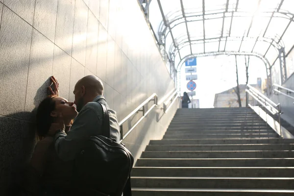 Um jovem casal está de pé nas escadas da passagem subterrânea perto da parede. Momento de beijo. Lugar para o seu texto. — Fotografia de Stock