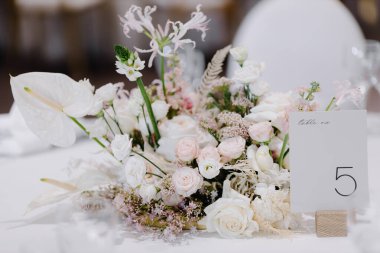 Düğün yemeği için süslü bir masada beş numara. Şölen sofrası kurulumu. Taze çiçekli beyaz düğün dekoru.