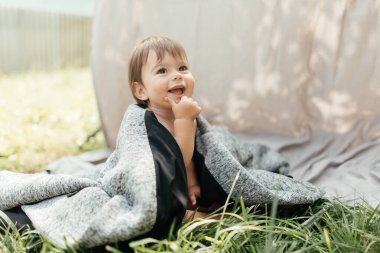 Küçük bir çocuk annesinin paltosuyla çimlerin üzerinde oturuyor. Yüksek kalite fotoğraf