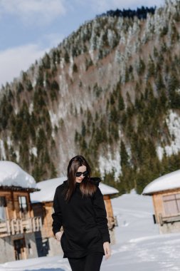  Siyah giyen genç kız kış dağlarının arka planında poz veriyor. Yüksek kalite fotoğraf