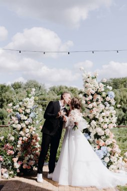  Güzel gelin ve damat, taze beyaz ve pembe çiçeklerin düğün töreninde öpüşüyor. Açık hava kutlamalarının tasarımı ve organizasyonu. Yüksek kalite fotoğraf