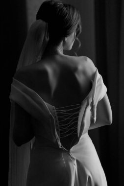 Gelin, arkası açık bir elbiseyle pencerede duruyor. siyah beyaz fotoğraf. Yüksek kalite fotoğraf