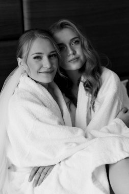 Genç güzel mankenler beyaz önlüklerle yatakta otururlar. Siyah beyaz fotoğraf. Yüksek kalite fotoğraf