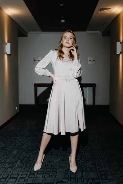 Krásná a stylová mladá dívka v šedých šatech pózuje v hotelové chodbě — Stock fotografie