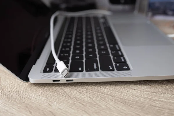 Charging battery laptop. Modern USB C port for fast charge. White cable plugged in laptop close-up view. High quality photo