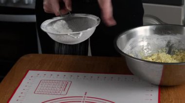 Demir bir elek tutan ve hamur halısı olan bir masada un elleyen iki çift kadın eli yakın çekim. Yüksek kalite 4k görüntü