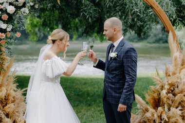  Beyaz elbiseli gelin ve kemerin arkasında da takım elbiseli bir damat bardaklarını çırpıyor. Kapatın. Yüksek kalite fotoğraf