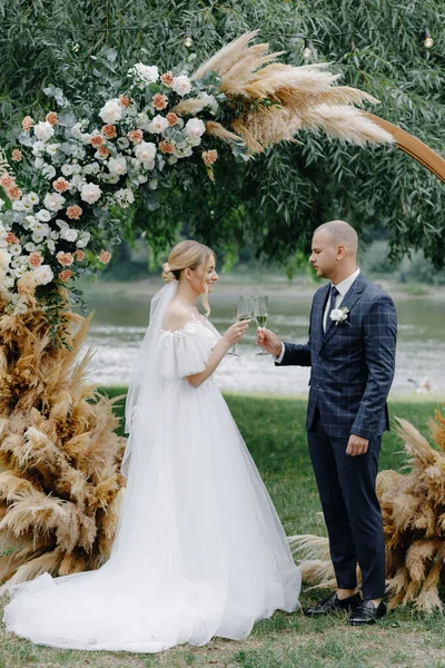 Novia Vestido Blanco Novio Traje Tintineo Gafas Fondo Del Arco — Foto de Stock