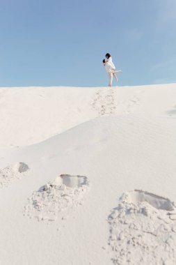  Genç çift kumlu bir yamacın tepesinde mavi bir gökyüzüne sarılıyor. Mesajın için yer aç. Yüksek kalite fotoğraf