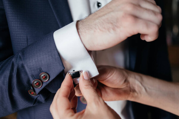 Women's hands fasten cufflinks on the cuffs of a man's shirt. Close up. High quality photo