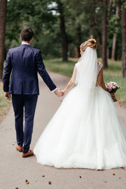 Portrait of the bride and groom from the back walking through the park. High quality photo