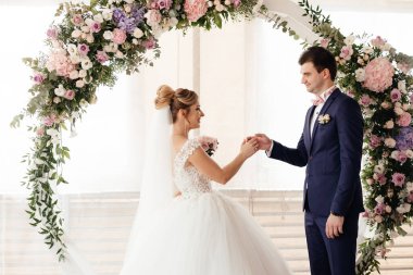  Gelin, törende damada yüzüğü takar ve yuvarlak bir gül kemerinin arkaplanına yaslanır. Yüksek kalite fotoğraf