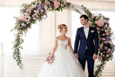 Gelin ve damat düğün töreninde kemerin yanında durur ve birbirlerine bakarlar. Yüksek kalite fotoğraf