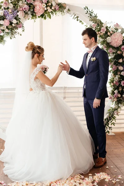  Gelin, törende damada yüzüğü takar ve yuvarlak bir gül kemerinin arkaplanına yaslanır. Vertycal fotoğraf. Yüksek kalite fotoğraf