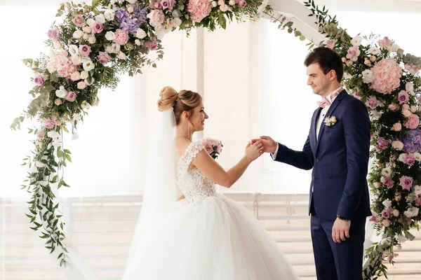  Gelin, törende damada yüzüğü takar ve yuvarlak bir gül kemerinin arkaplanına yaslanır. Yüksek kalite fotoğraf