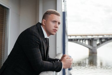 Klasik elbiseli damat balkonda dikiliyor, başka tarafa bakıyor. Damadın sabahı. Düşünceli damat balkonda duruyor. Yüksek kalite fotoğraf