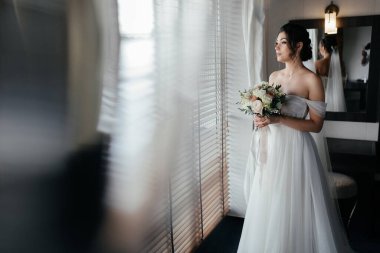 Güzel gelin. Genç, çok ırklı Asyalı beyaz bir model beyaz bir odaya karşı bir gelin gibi büyük bir pencereyle başka tarafa bakıyor. Yüksek kalite fotoğraf