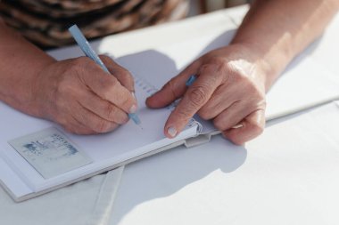Fotoğrafın yanında elinde kalem olan yaşlı bir kadının elleri. Yüksek kalite fotoğraf