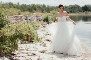  Genç gelin güzel bir gelinlikle gölün kıyısında yürüyor. Yüksek kalite fotoğraf