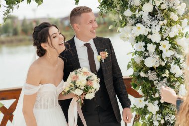 Newlyweds are smiling on the background of an arch of flowers. High quality photo