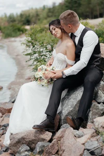 Güzel yeni evliler taşların üzerine oturur ve sarılırlar. Yüksek kalite fotoğraf