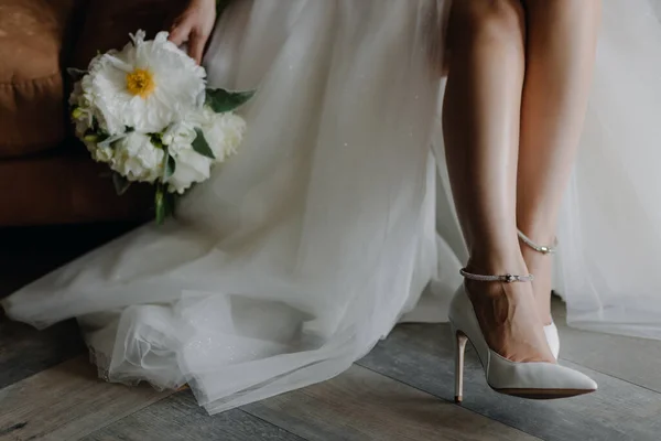 Horizontal close-up photo of the bride\'s feet in shoes on the floor. Blurred wedding bouquet. High quality photo. High quality photo