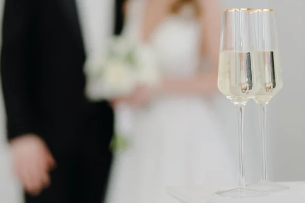 Two glasses of champagne stand on the table against the background of newlyweds in love at the wedding ceremony. High quality photo