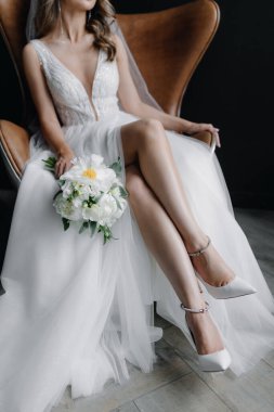 Bir sandalyede otururken gelinin ayaklarının yerdeki ayakkabılarla dikey yakın plan fotoğrafı. Elinde bir düğün buketi tutuyor. Yüksek kalite fotoğraf