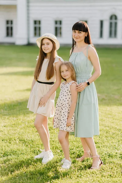 Mom and two little daughters in dresses pose in front of the camera in summer nature and look into the camera. A happy family. High quality photo