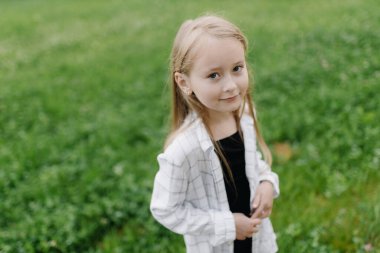 Smiling cute little girl on the background of green trees on a summer day. Copy space. High quality photo