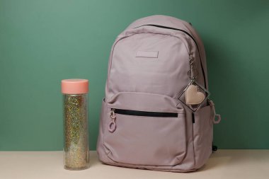 A school backpack with a bottle of water on a table on a green background. Preparation for school. High quality photo