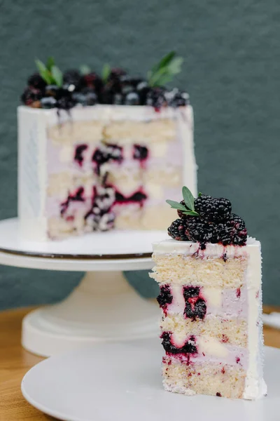 A piece of cut cake with berries on a white plate on a blurred cake background. High quality photo