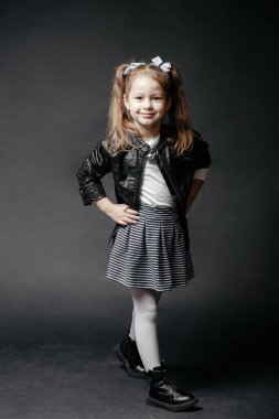 Siyah deri ceketli gülümseyen bir kızın stüdyo portresi, siyah arka planda elbise ve çizmeler. Yüksek kalite fotoğraf