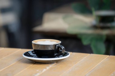 Masanın üzerinde duran kapuçinolu siyah fincan cam duvara yansıyor.