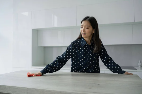 Mujer asiática limpia y limpia la mesa con un paño de microfibra en la cocina. Una mujer hace tareas domésticas alrededor de la casa. El concepto de gestión del hogar. — Foto de Stock